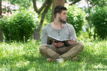 Adult Muslim Man Is Reading The Koran Outside In A Park