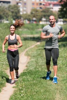 Young Couple Running In Wooded Forest Area - Training And Exercising For Trail Run Marathon Endurance - Fitness Healthy Lifestyle Concept