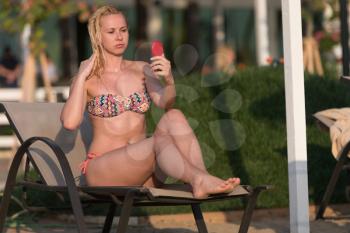 Attractive Young Woman Chilling in Chair at Sea Shore - Girl Looking at Herself in Small Mirror
