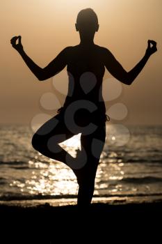 Young Healthy Woman Practicing Yoga Fitness Exercise on the Beach at Sunset - Healthy Lifestyle Concept - Copy Space Text