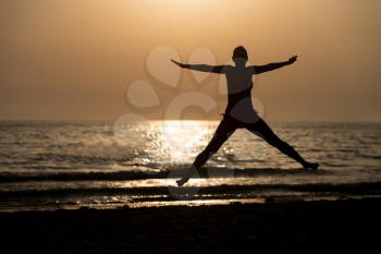 Silhouette of Woman With Raised Hands And Jumping Around on the Beach at Sunset - Copy Space Text
