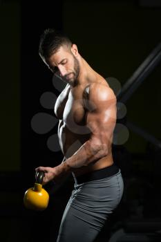 Young Man Working Out With Kettle Bell In A Dark Gym - Bodybuilder Doing Heavy Weight Exercise With Kettle-bell