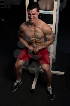 Handsome Man Sitting Strong In The Gym And Flexing Muscles - Muscular Athletic Bodybuilder Fitness Model Posing After Exercises