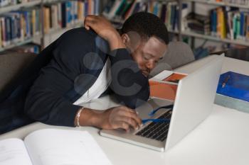 Sleeping African Student Sitting And Leaning On Pile Of Books In College - Shallow Depth Of Field