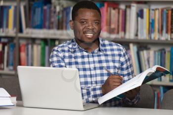 In The Library - Handsome African Male Student With Laptop And Books Working In A High School - University Library - Shallow Depth Of Field