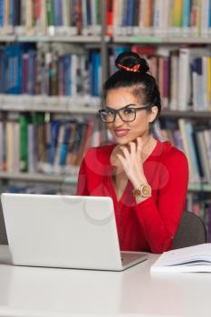 In The Library - Pretty Female Student With Laptop And Books Working In A High School Or University Library - Shallow Depth Of Field