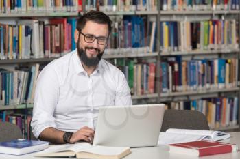 In The Library - Handsome Male Student With Laptop And Books Working In A High School - University Library - Shallow Depth Of Field