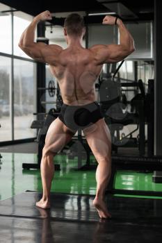 Handsome Young Man Standing Strong In The Gym And Flexing Muscles - Muscular Athletic Bodybuilder Fitness Model Posing After Exercises