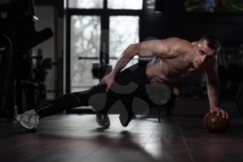 Young Man Athlete Doing Pushups On Ball With One Hand As Part Of Bodybuilding Training