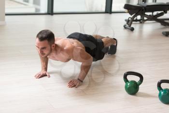 Healthy Man Athlete Doing Pushups Workout With Kettle Bell In A Gym - Kettle-bell Exercise