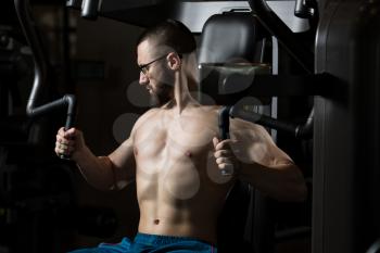 Handsome Muscular Fitness Man Wearing Glasses Doing Heavy Weight Exercise For Chest On Machine With Cable In The Gym