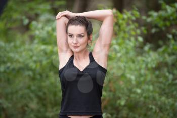 Young Woman Stretching Before Running In Wooded Forest Area - Training And Exercising For Trail Run Marathon Endurance - Fitness Healthy Lifestyle Concept