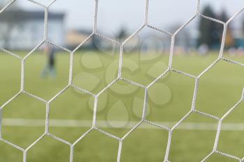 Soccer or Football Net Background - View From Behind the Goal With Blurred Stadium and Field Pitch