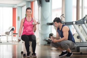 Personal Trainer Showing Young Woman How To Train Biceps Exercise With Dumbbells In A Health And Fitness Concept