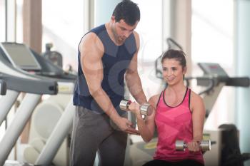 Personal Trainer Showing Young Woman How To Train Biceps Exercise With Dumbbells In A Health And Fitness Concept