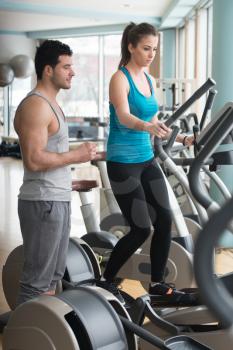 Group Of People Exercising On Elliptical Walker In Gym Or Fitness Club While Personal Trainer With Clipboard Watching Them - Group Of Woman And Men Exercising To Gain More Fitness