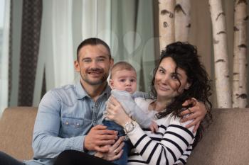 Happy Family Father and Mother Playing With a Baby at Home on the Sofa