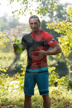 Muscular Man Resting After Exercise And Drinking From Shaker Outdoors In Nature