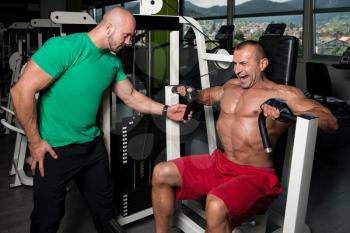 Mature Man Working Out In Gym - Doing Chest Exercise On Machine With Help Of His Trainer