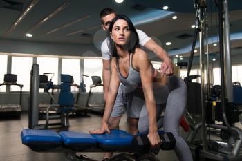 Personal Trainer Showing Young Woman How To Train Back With Dumbell In The Gym