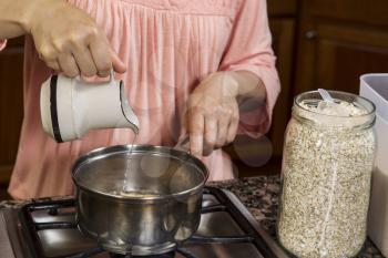 Women pouring water into oatmeal and wheat germ into stainless steel pan on stove