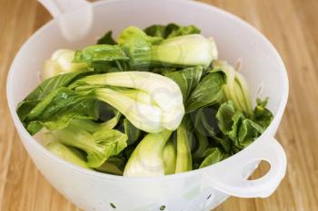 Closeup horizontal photo of washed Chinese Choy vegetable in plastic drain bowl on natural bamboo wood
