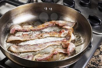 Frying bacon in stainless steel frying pan on stove top