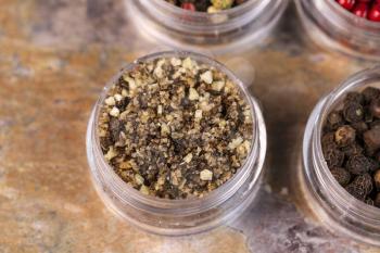 Horizontal top focus shot of brown coarse sea salt and peppercorns in small containers on stone surface