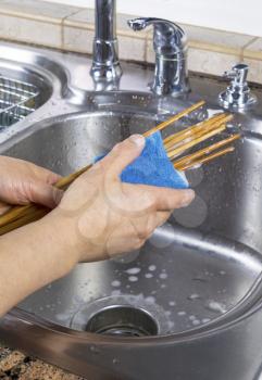Vertical photo of female hands cleaning bamboo chopsticks with kitchen faucet sink in background