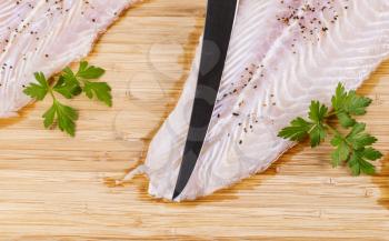 tip of fillet knife on top of white skinless fish with spices and parsley on bamboo board