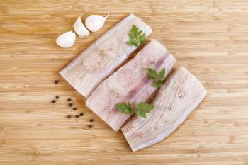 Horizontal photo of white fish fillets, parsley, garlic and pepper salts on Natural Bamboo Wood background