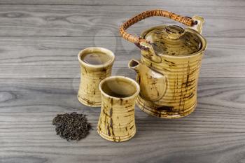 Fresh pot of green tea with dried green tea leafs and cups on white ash wood background