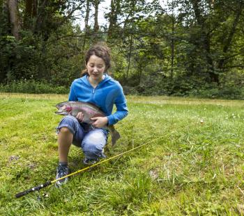 Young girl with eyes closed giving thanks after landing a large trout with woods in background