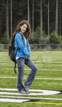 Young girl holding notepads on soccer field with woods in background
