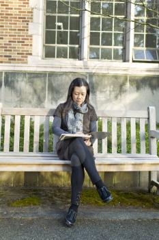 Asian women sitting on bench looking at note book pads with brick building in background