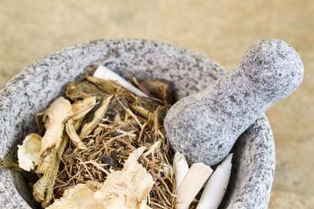 Closeup horizontal photo of a natural stone pestle in stone bowl filled with Chinese herbs used for medicine
