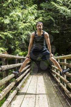 Athletic young man straddling walkway bridge into woods