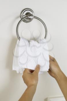 Vertical photo of female hands putting clean white towel on wall hook ring in bathroom 