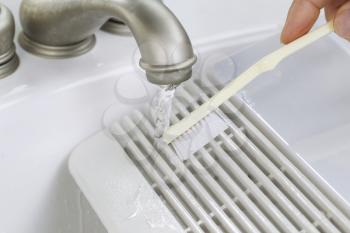 Close up horizontal photo of female hand with tooth brush cleaning bathroom fan vent cover in bathroom sink 