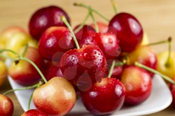 Closeup horizontal photo of Rainier cherries, with water drops, in white dish on natural bamboo board