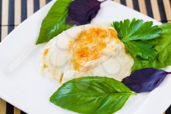 Closeup horizontal photo of baked stuffed sole fish, sweet basil, inside white square plate on bamboo placemat 