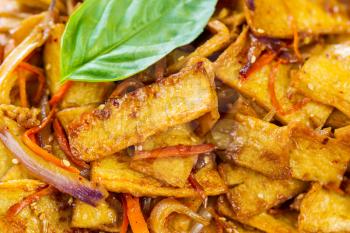Horizontal photo of fried tofu, carrots, onions with spices, sauce and basil on top