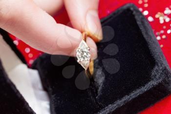 Horizontal photo of female fingers picking up diamond ring from Jewelry box on red background 