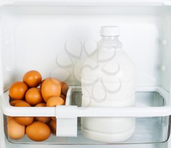 Photo of Fresh brown organic eggs and milk on inside of refrigerator door shelf