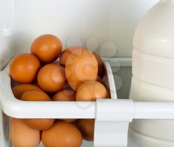 Closeup photo of Fresh brown organic eggs and partial milk container on inside of refrigerator door shelf