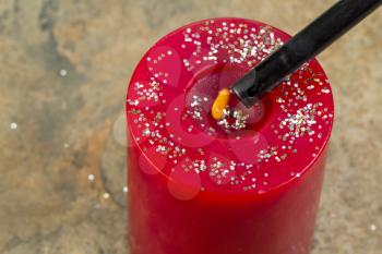 Horizontal photo of red holiday candle being light with fire starter on stone background 