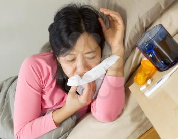Photo of mature woman blowing her nose with a tissue while lying in bed sick