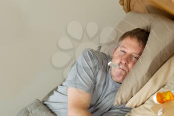 Horizontal photo of mature man with thermometer in mouth while lying in bed 
