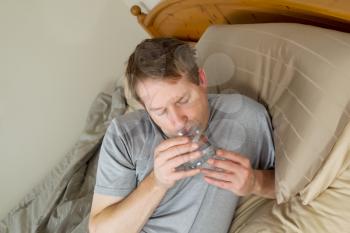 Horizontal photo of mature man drinking water in bed 