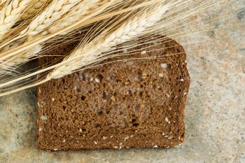 Horizontal photo of a single slice of sweet dark whole grain bread with dried wheat stalks on natural stone counter top 